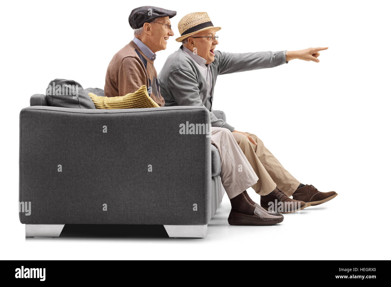Two mature men sitting on a couch with one of them pointing isolated on white background Stock Photo