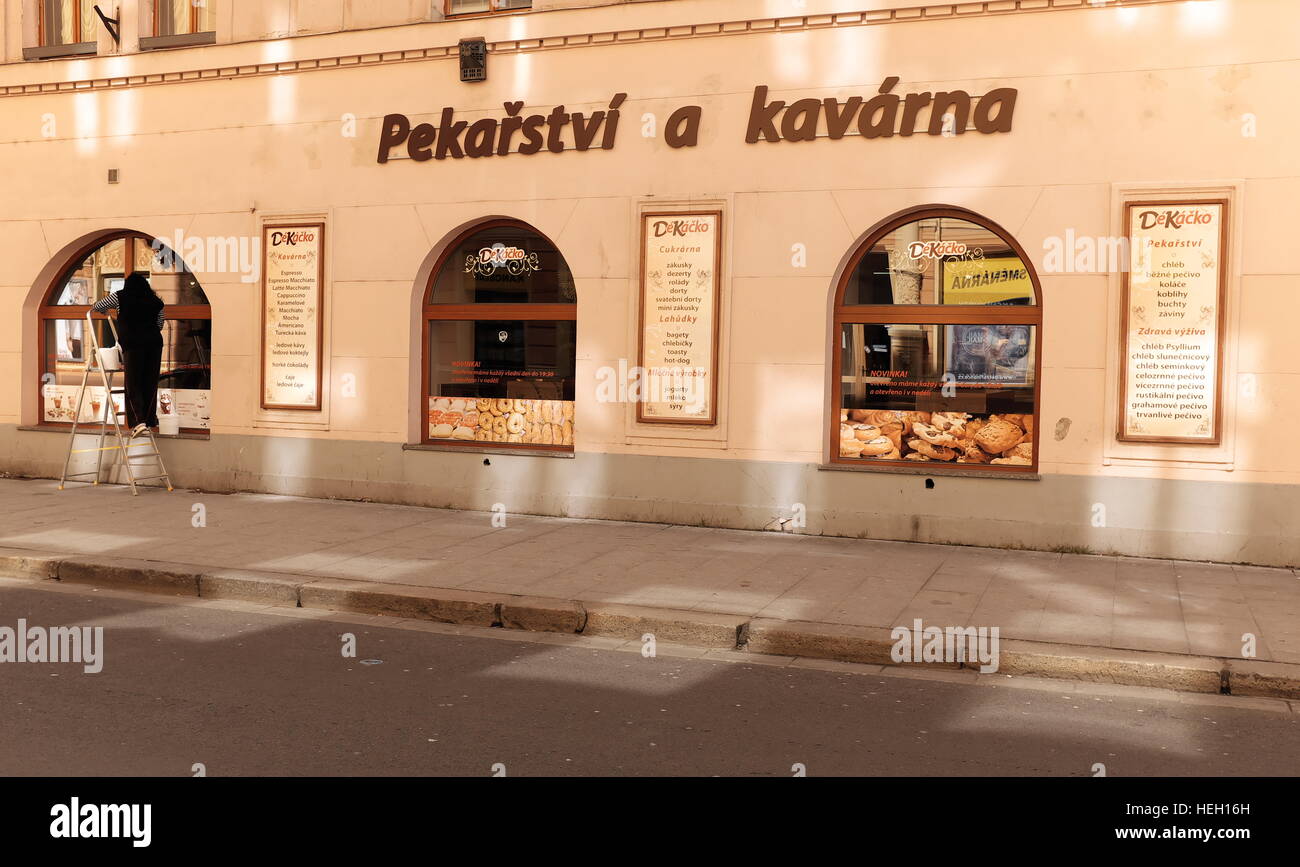 A woman washed windows of a bakery and cafe storefront at sunset in Ceske Budejovice, Czech Republic, in 2016 Stock Photo