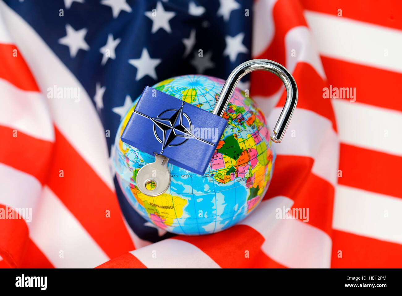 Weltkugel mit einem offenen Vorhaengeschloss und Nato-Schriftzug auf einer USA-Fahne, amerikanische Sicherheitspolitik im Wandel Stock Photo