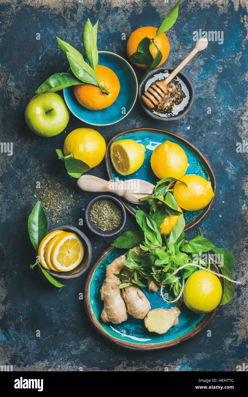 Ingredients for making natural hot drink in blue ceramic plates over dark blue shabby background. Oranges, mint, lemon, ginger, honey and apple, top v Stock Photo