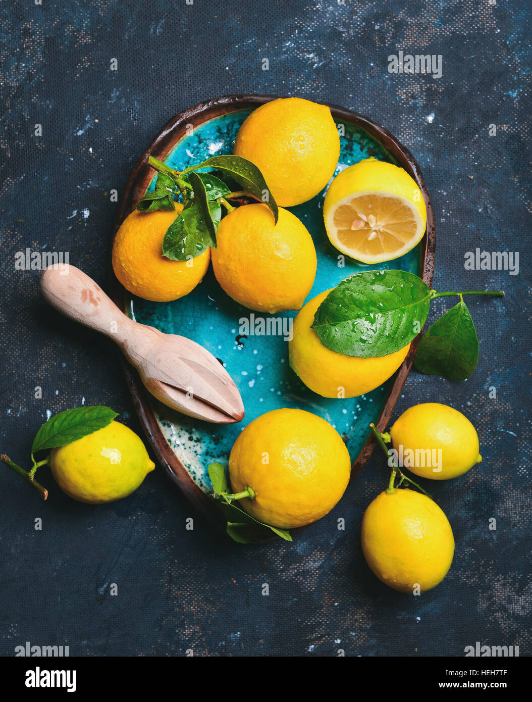 Freshly picked lemons with leaves in blue ceramic plate over dark blue shabby background, top view, vertical composition Stock Photo