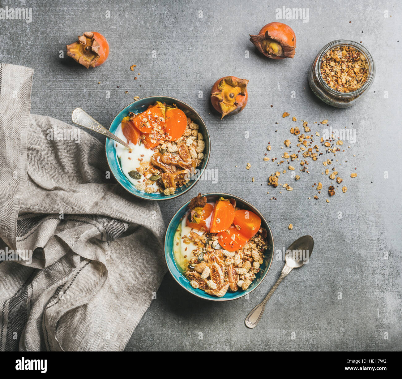 Healthy vegetarian breakfast bowls. Oatmeal and quinoa granola with yogurt, dried fruit, seeds, honey and persimmon in colorful bowls over grey concre Stock Photo