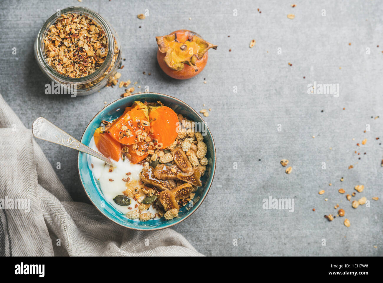 Healthy breakfast concept. Oatmeal, quinoa granola with yogurt, dried fruit, seeds, honey, persimmon in bowl over grey concrete background, top view, Stock Photo