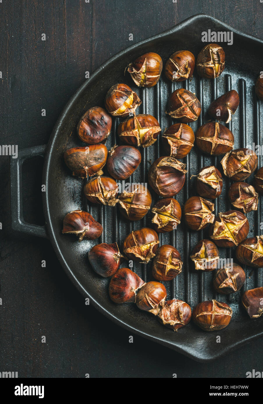 Roasted chestnuts in cast iron grilling pan over dark wooden background, top view, vertical composition Stock Photo