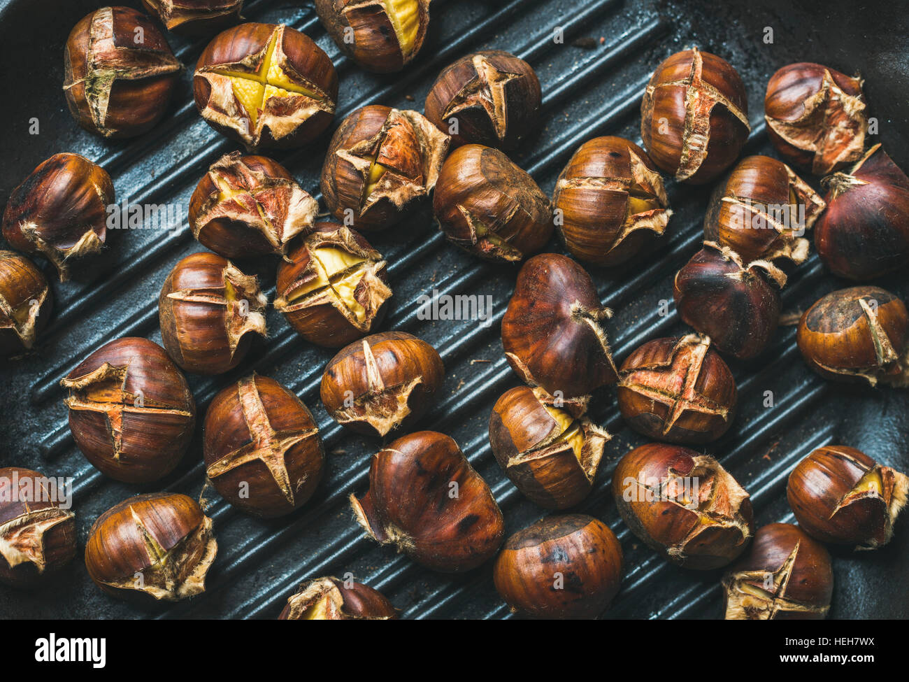 Close-up of roasted chestnuts over black cast iron grilling pan surface, top view, horizontal composition Stock Photo