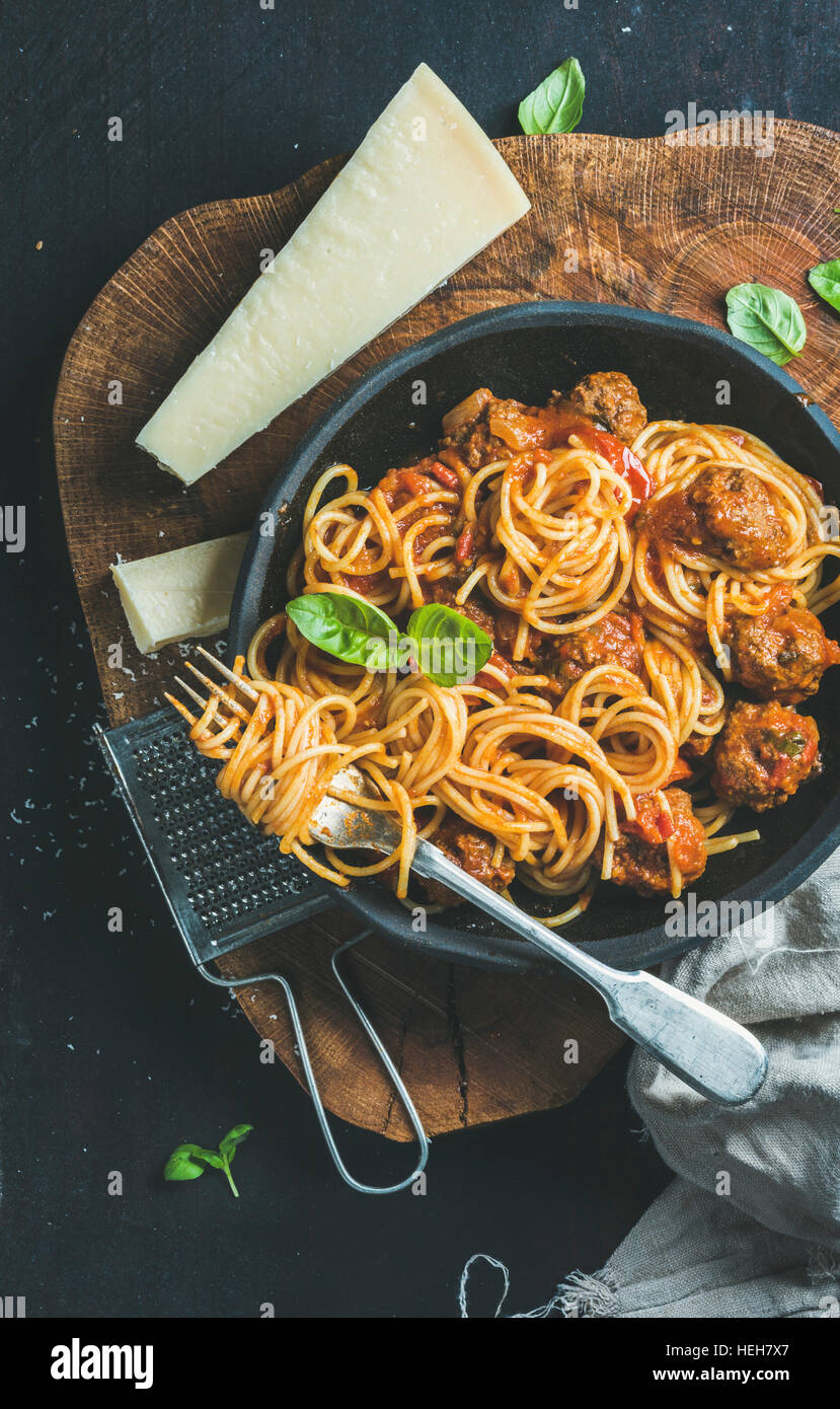 Italian pasta dinner. Spaghetti with meatballas, basil and parmesan cheese in black plate over dark rustic wood background, top view, Slow food concep Stock Photo