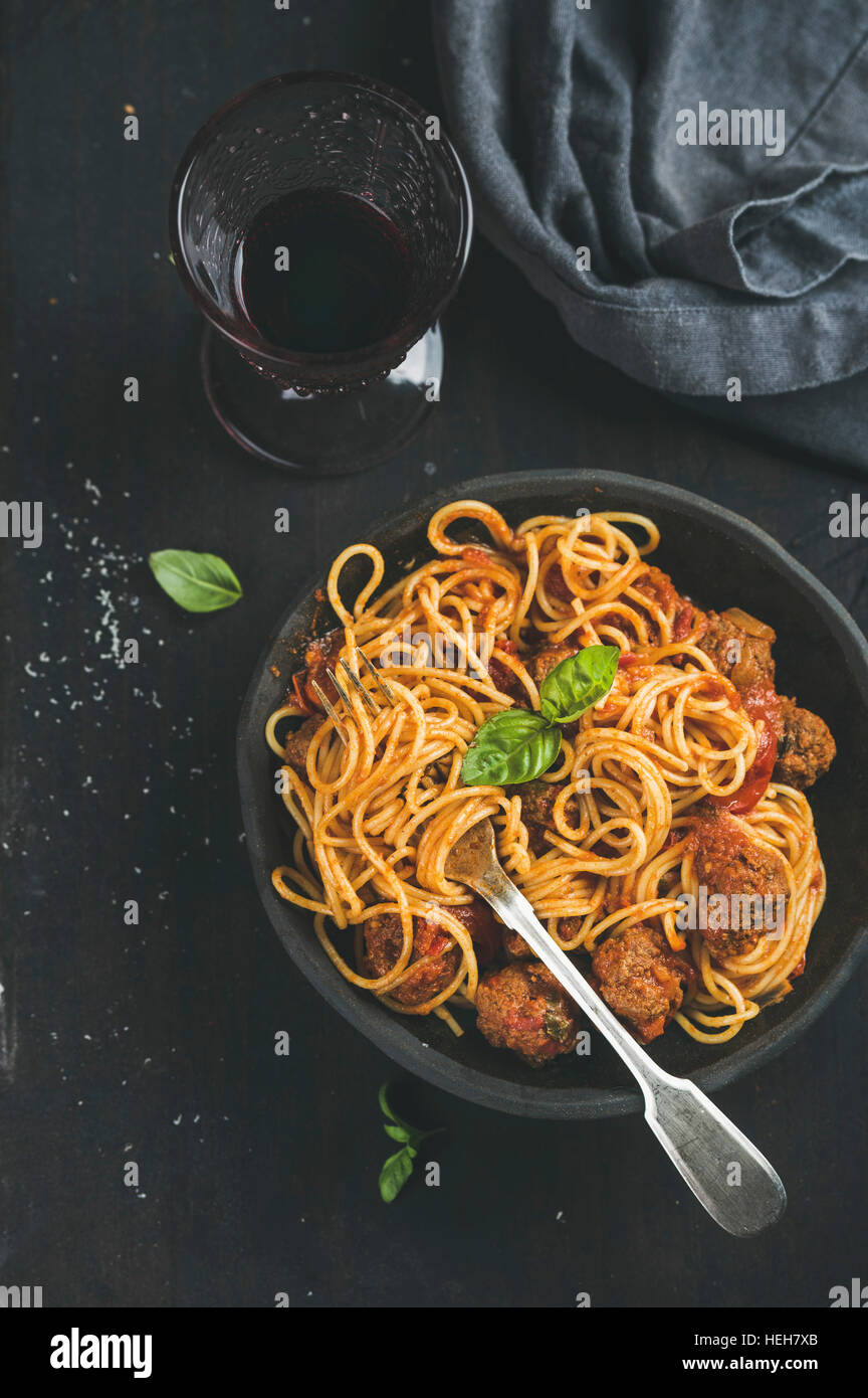 Italian pasta dinner. Spaghetti with meatballas, fresh basil leaves in dark plate and red wine in vintage glass over black background, top view. Slow Stock Photo