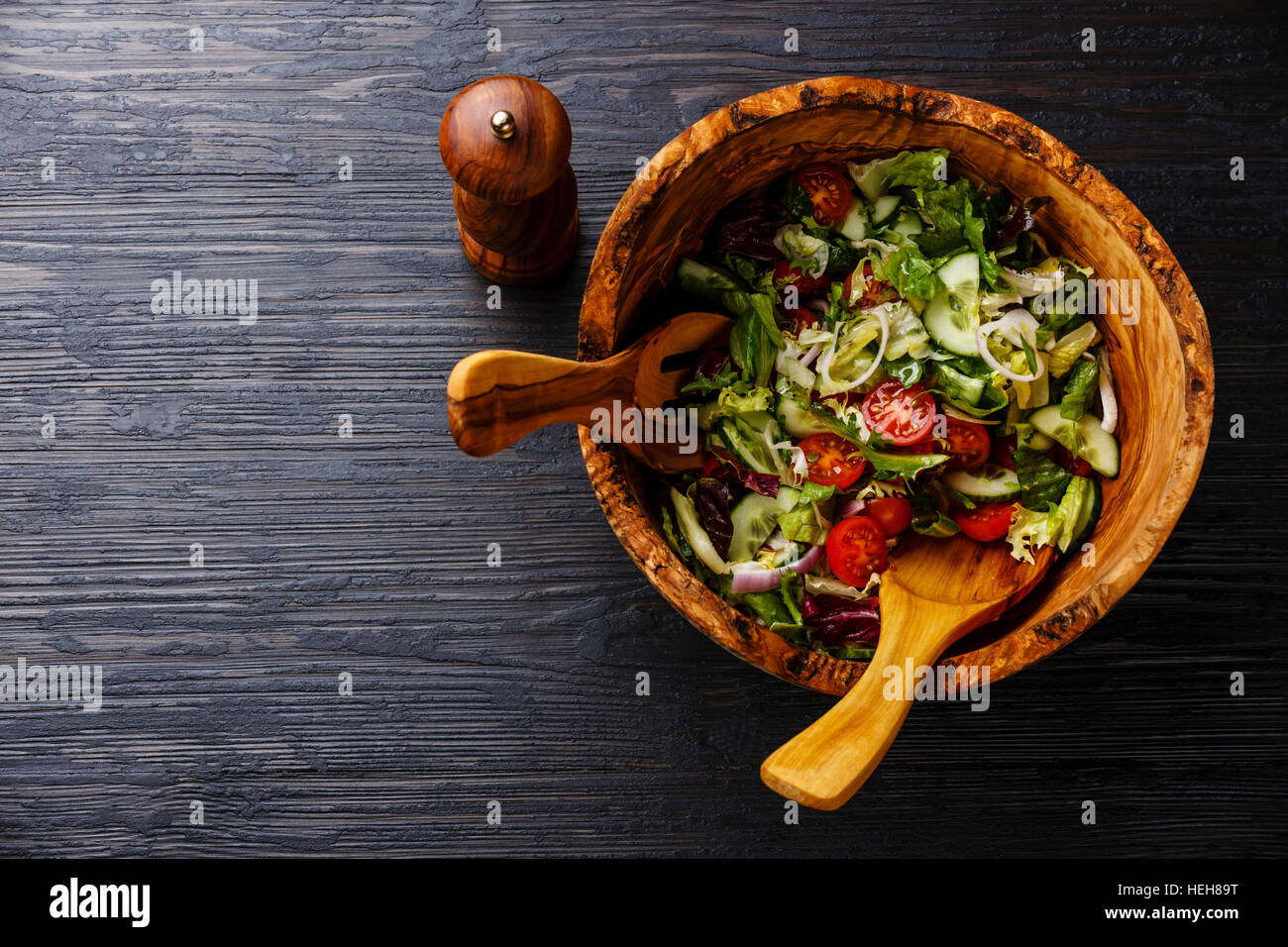 Fresh vegetable salad in olive wood bowl on black burned wooden background copy space Stock Photo