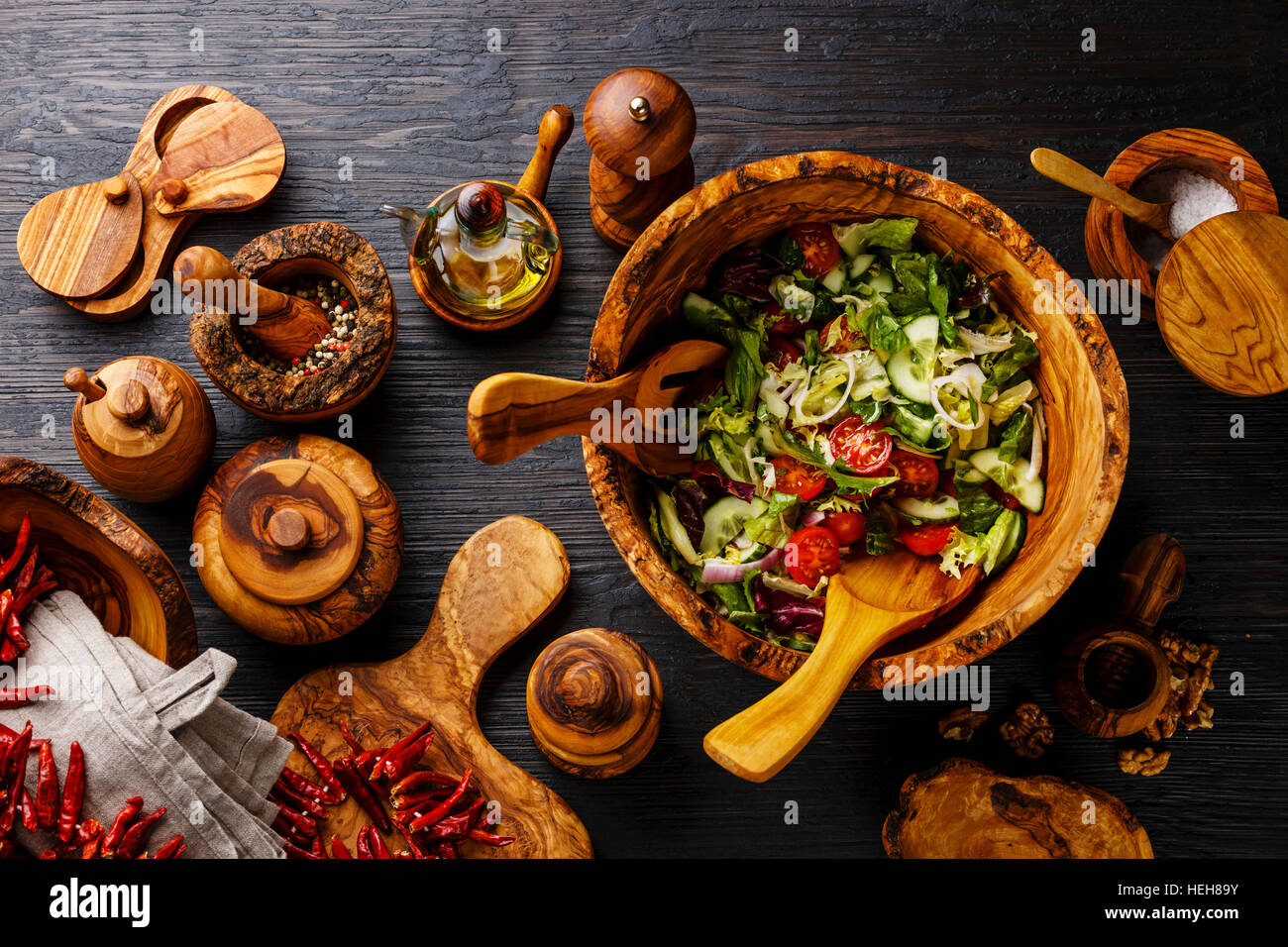 Fresh vegetable salad in olive wood bowl and wooden tableware on black burned wooden background Stock Photo