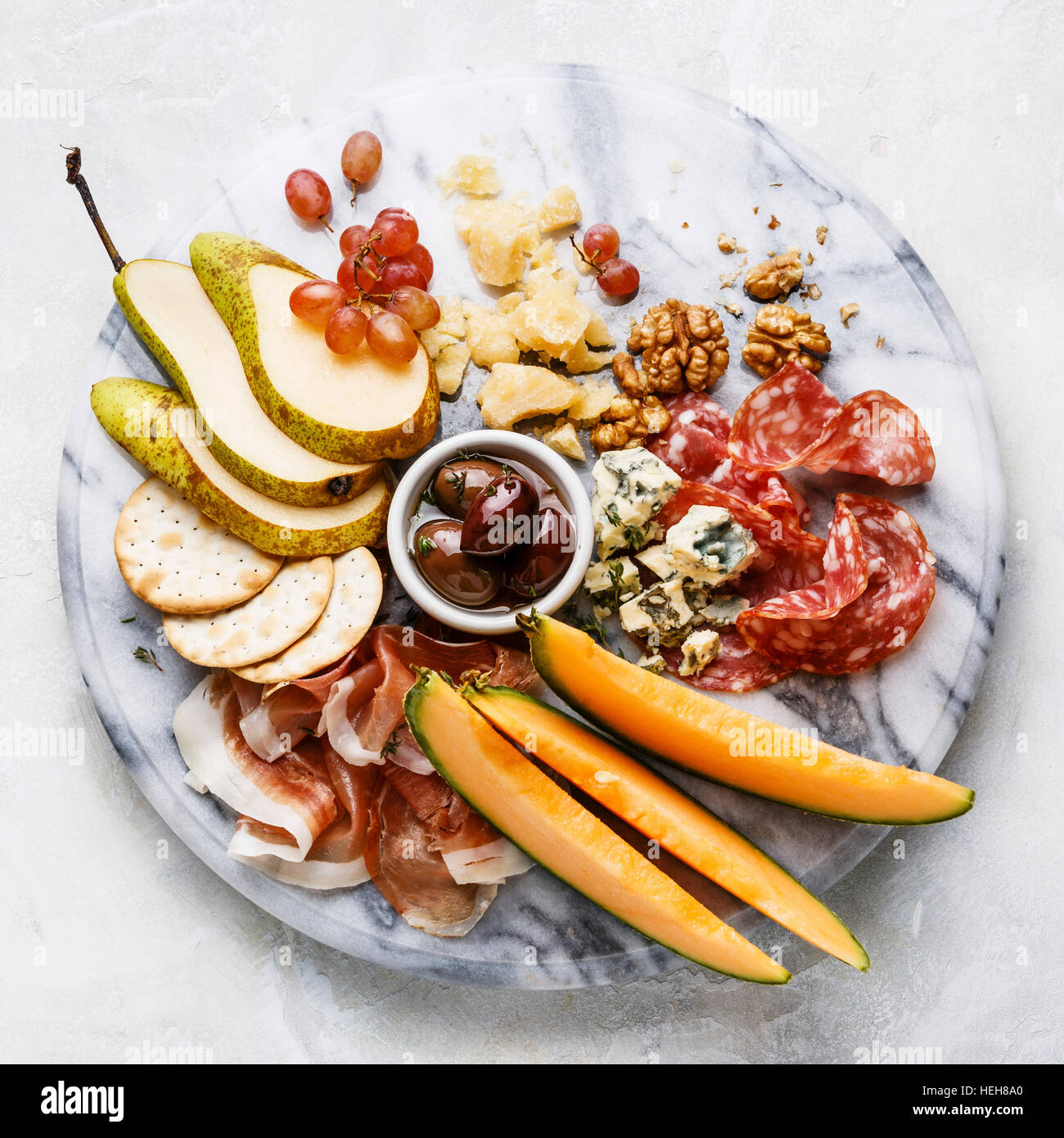 Meat and cheese plate antipasti snack with Prosciutto ham, Salami, Parmesan, Blue cheese, Cantaloupe melon and Olives on marble board Stock Photo