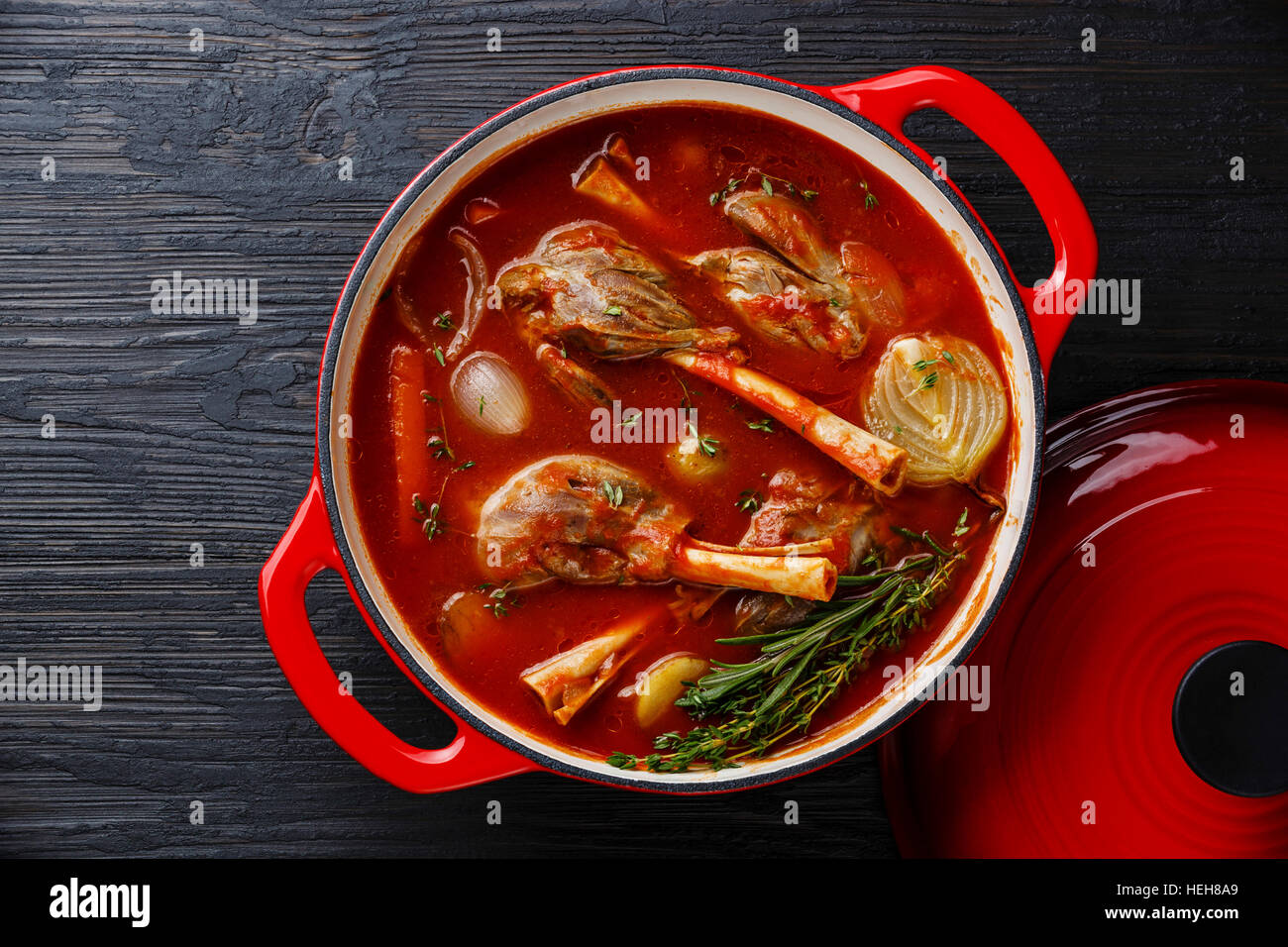 Stewed lamb on bone stewed in tomato sauce in cast iron pot on burned black wooden background Stock Photo