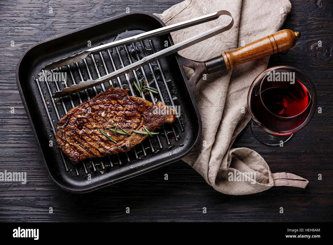 Grilled Steak Striploin in grill iron pan and red wine on black burned wooden background Stock Photo