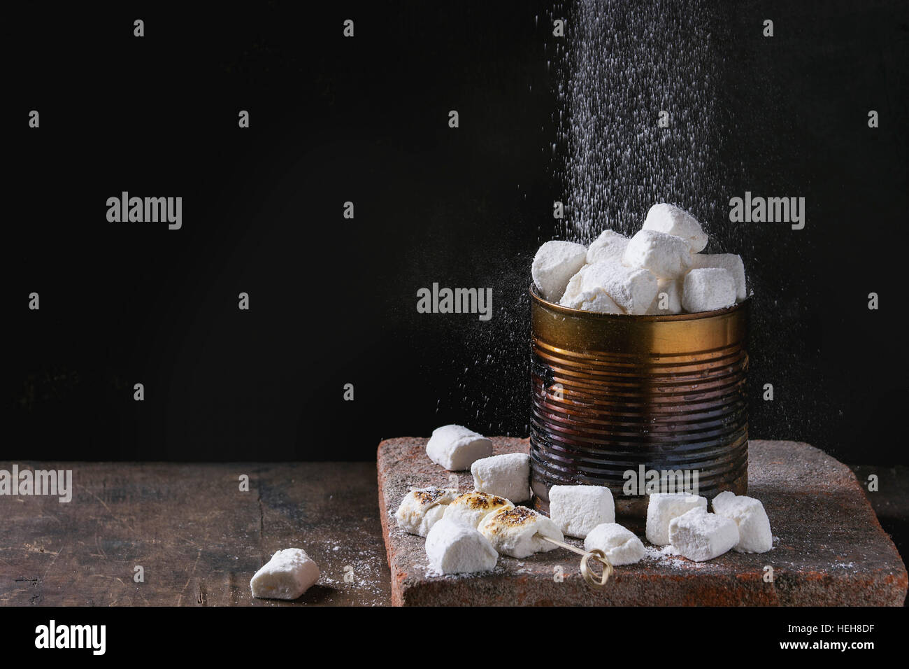 Heap of homemade vanilla marshmallow fresh and fried with sprinkling sugar powder in old tin can on terracotta board over dark wooden background. Copy Stock Photo