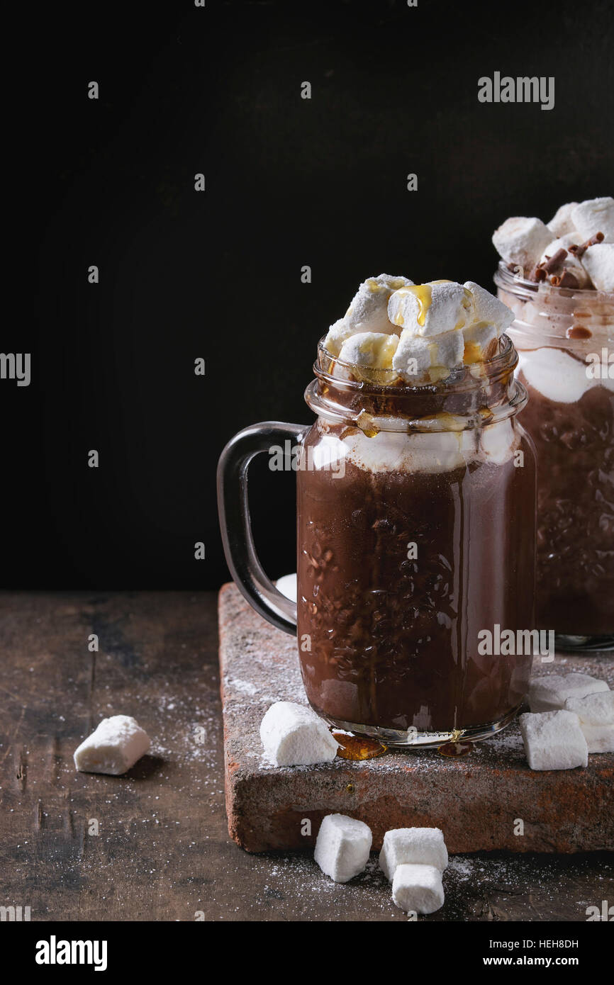 Hot chocolate with homemade marshmallow, chocolate chips and syrup in mason jars, standing on terracotta board over old dark wooden background. Copy s Stock Photo