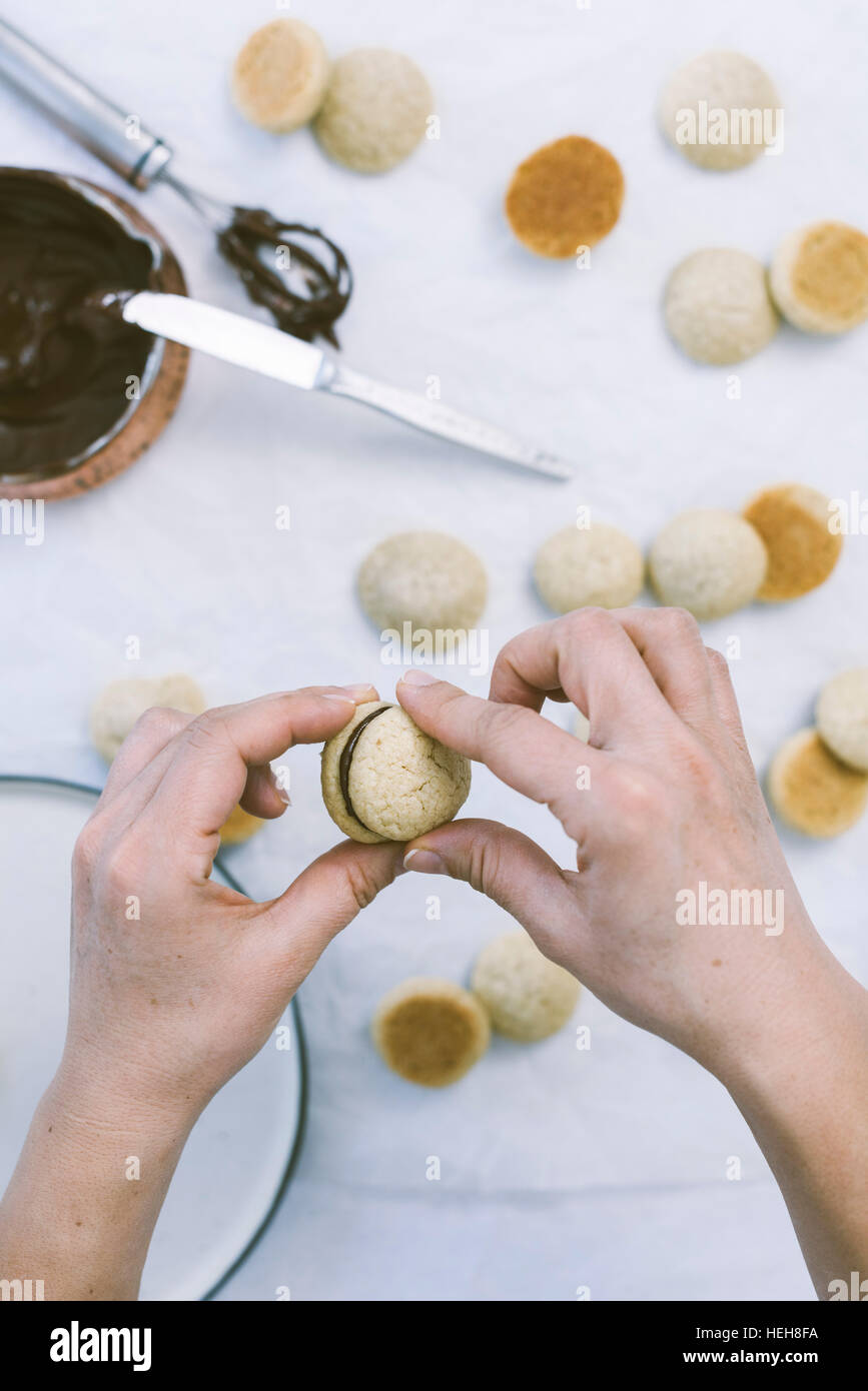 Hands forming sandwiches using two coconut sandwiches and melted chocolate between them Stock