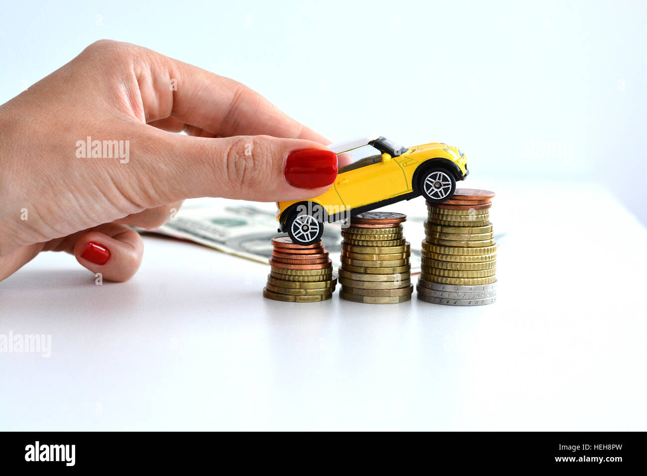 Woman hand pushing a toy car over a stack of coins Stock Photo