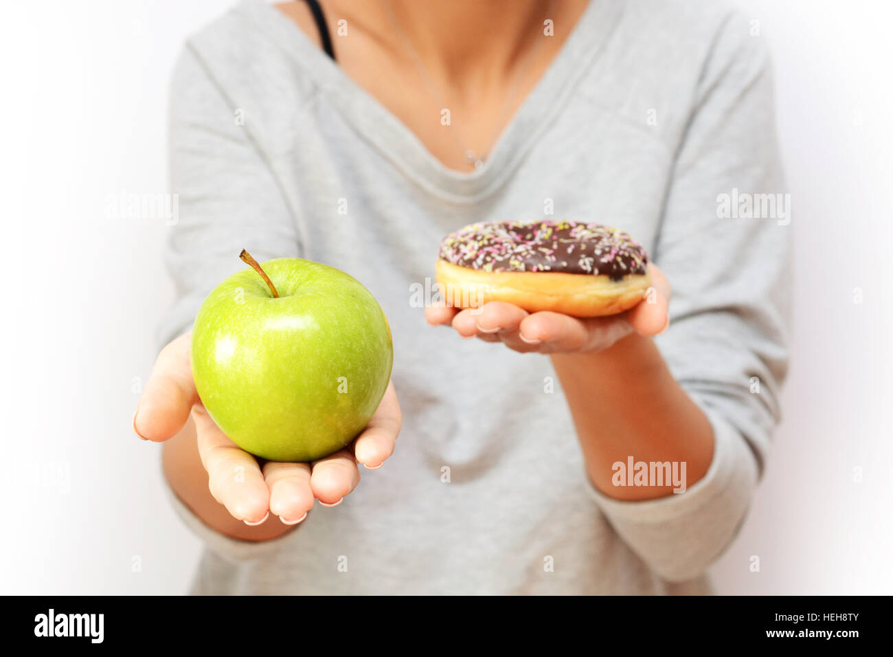 Healthy lifestyle or nutrition concept with young woman holding in hands an green apple and a donut Stock Photo