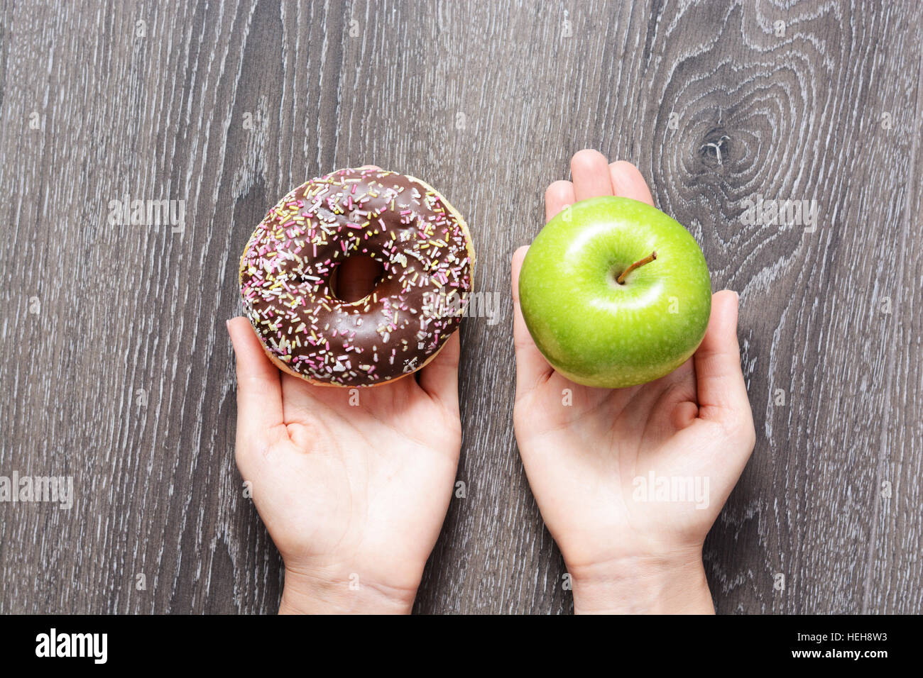 Healthy lifestyle or nutrition concept with young woman holding in hands an green apple and a donut Stock Photo