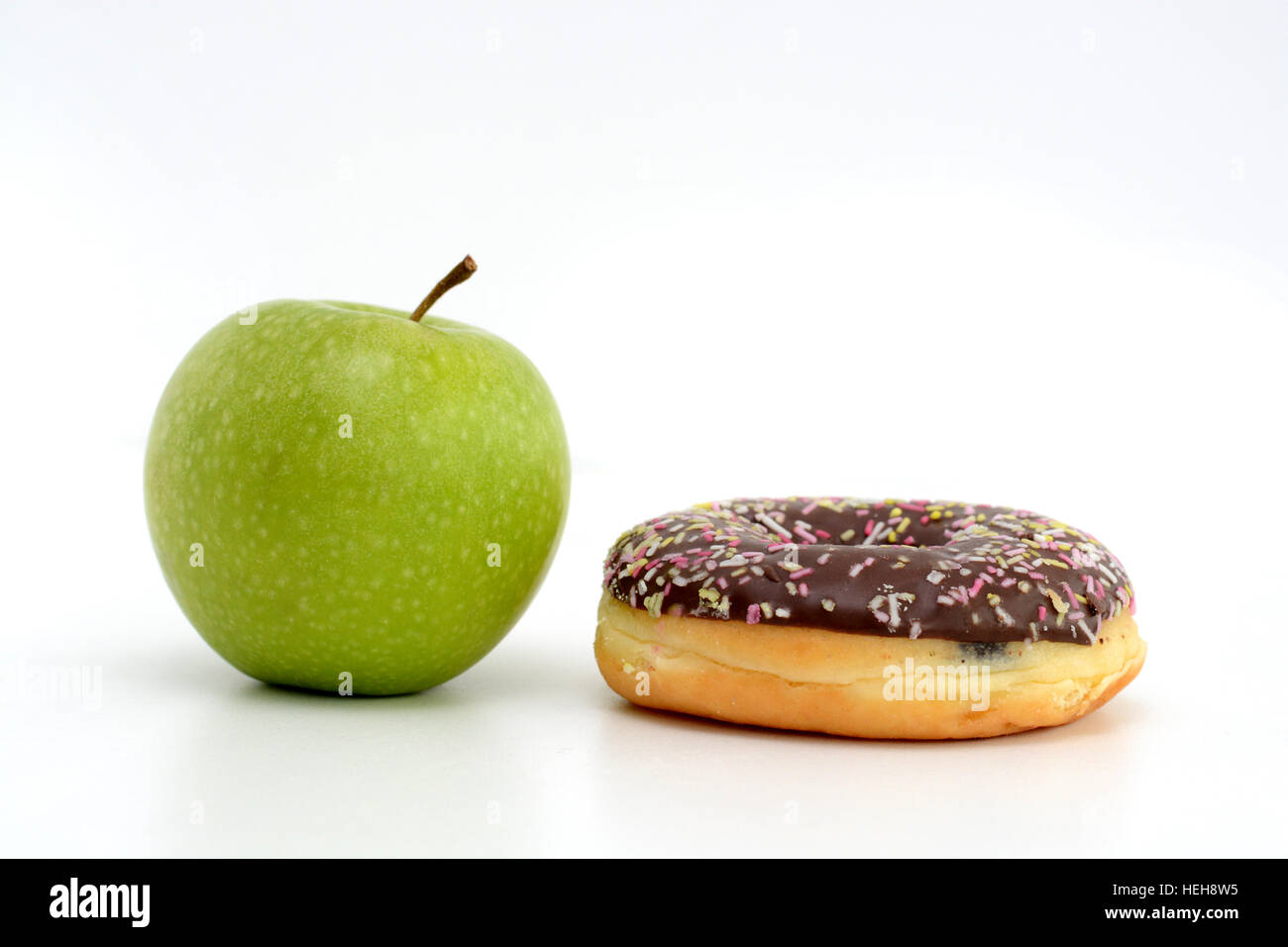 Choosing between healthy fruits and sweets. Green apple and tasty chocolate donut Stock Photo