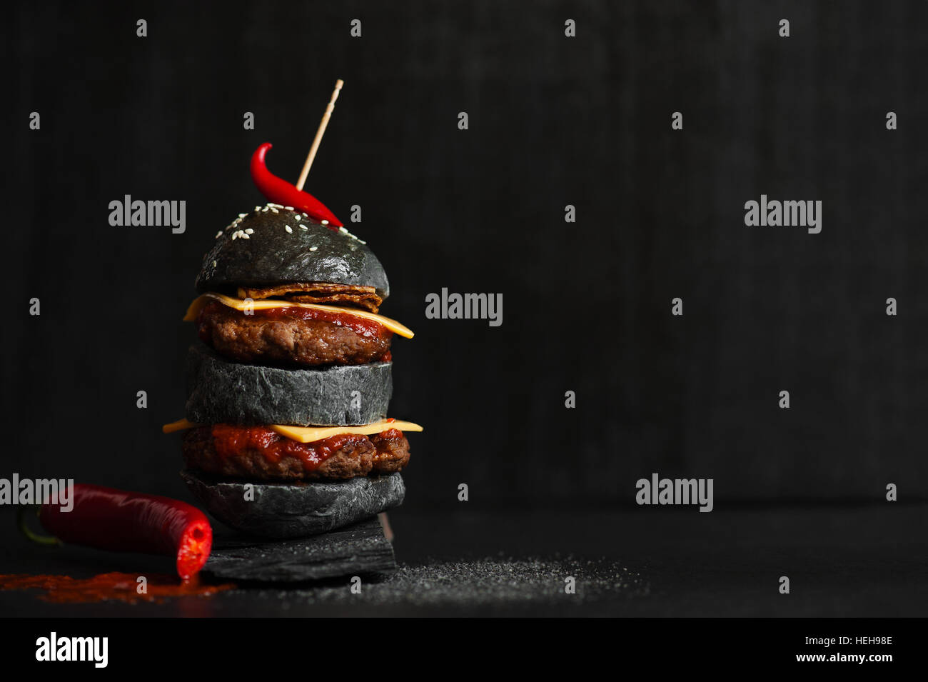 Black burger with meat, cheese, fried onion, tomato sauce and hot chili pepper on the black table Stock Photo