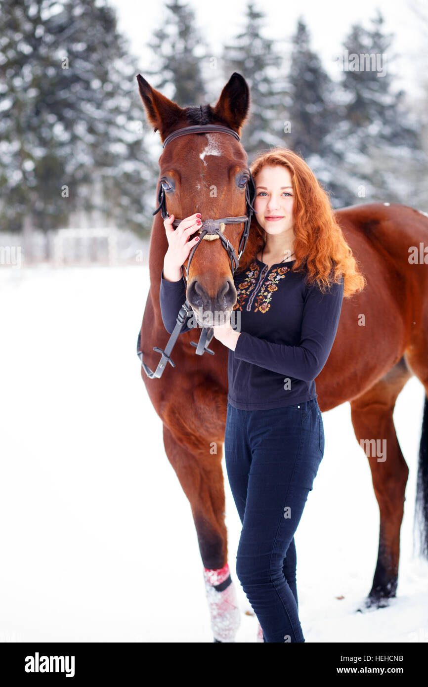 Young teenage girl standing with bay horse in winter park Stock Photo