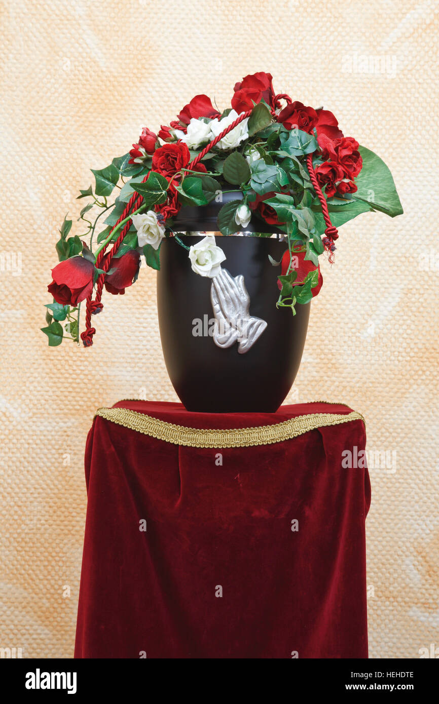 Urn decorated with hands clasped in prayer and artificial flowers Stock