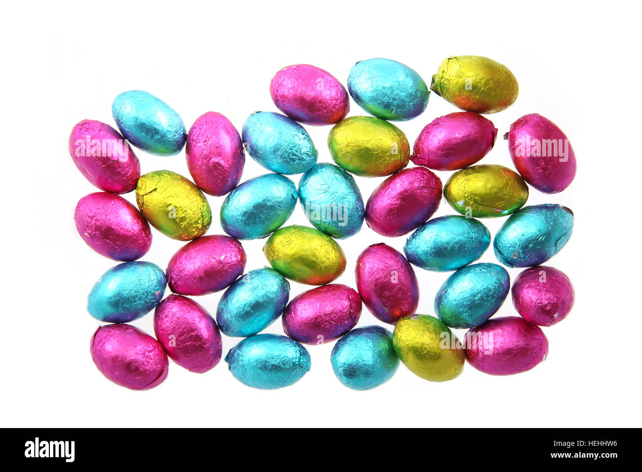 Pile of foil wrapped chocolate easter eggs in pink, blue & lime green with a white background. Stock Photo