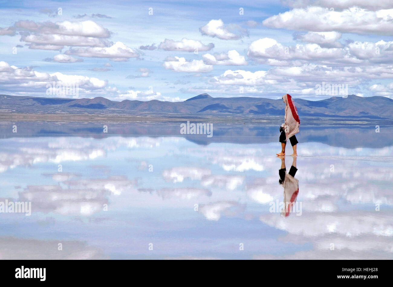 Woman walking in the clouds, mirror reflection in the water at the Uyuni Salt Flats Bolivia Stock Photo