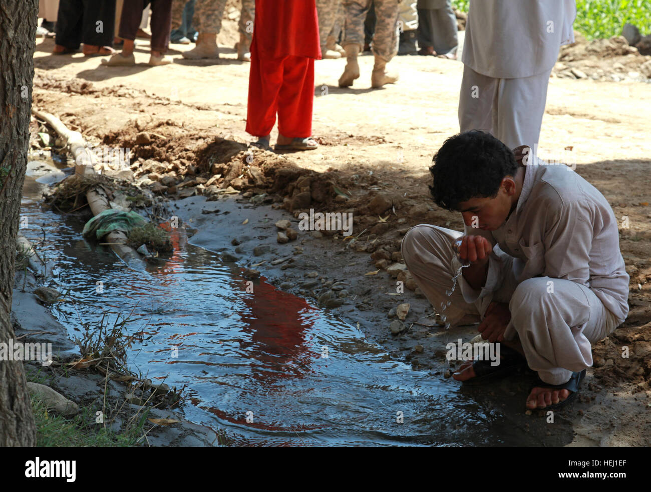 An Afghan boy drinks nonpotable water from a creek next to a dirt road