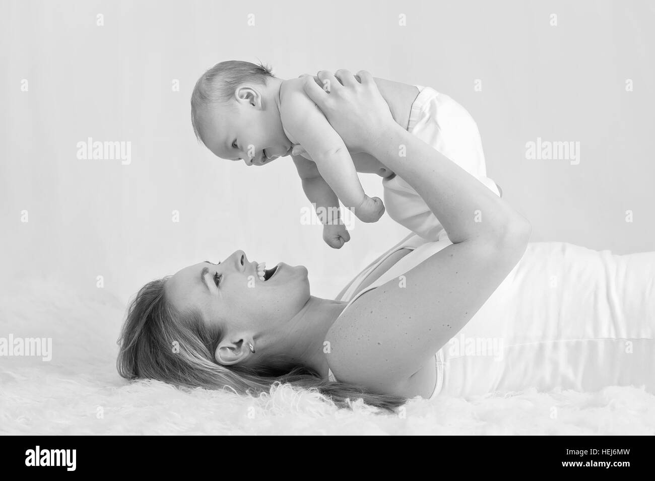 A black and white image of a mother laughing and playing with her baby boy. Stock Photo