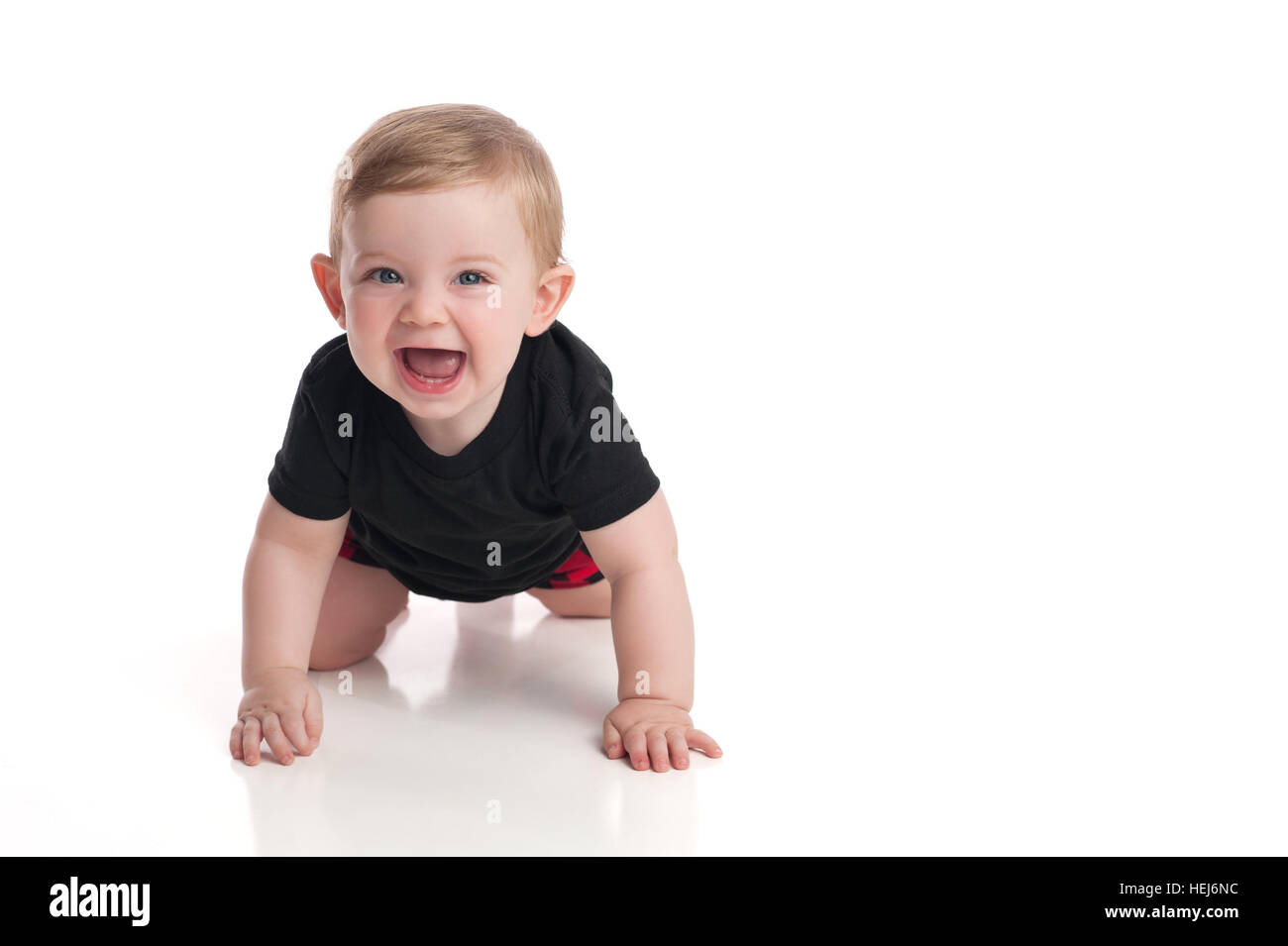 A laughing, eight month old, baby boy crawling toward the camera on a