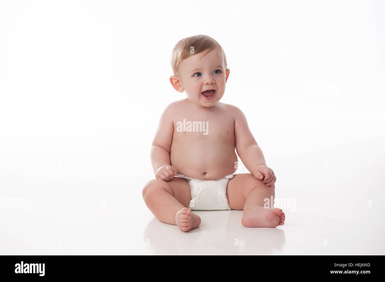 A smiling, eight month old, baby boy wearing a diaper and sitting on a