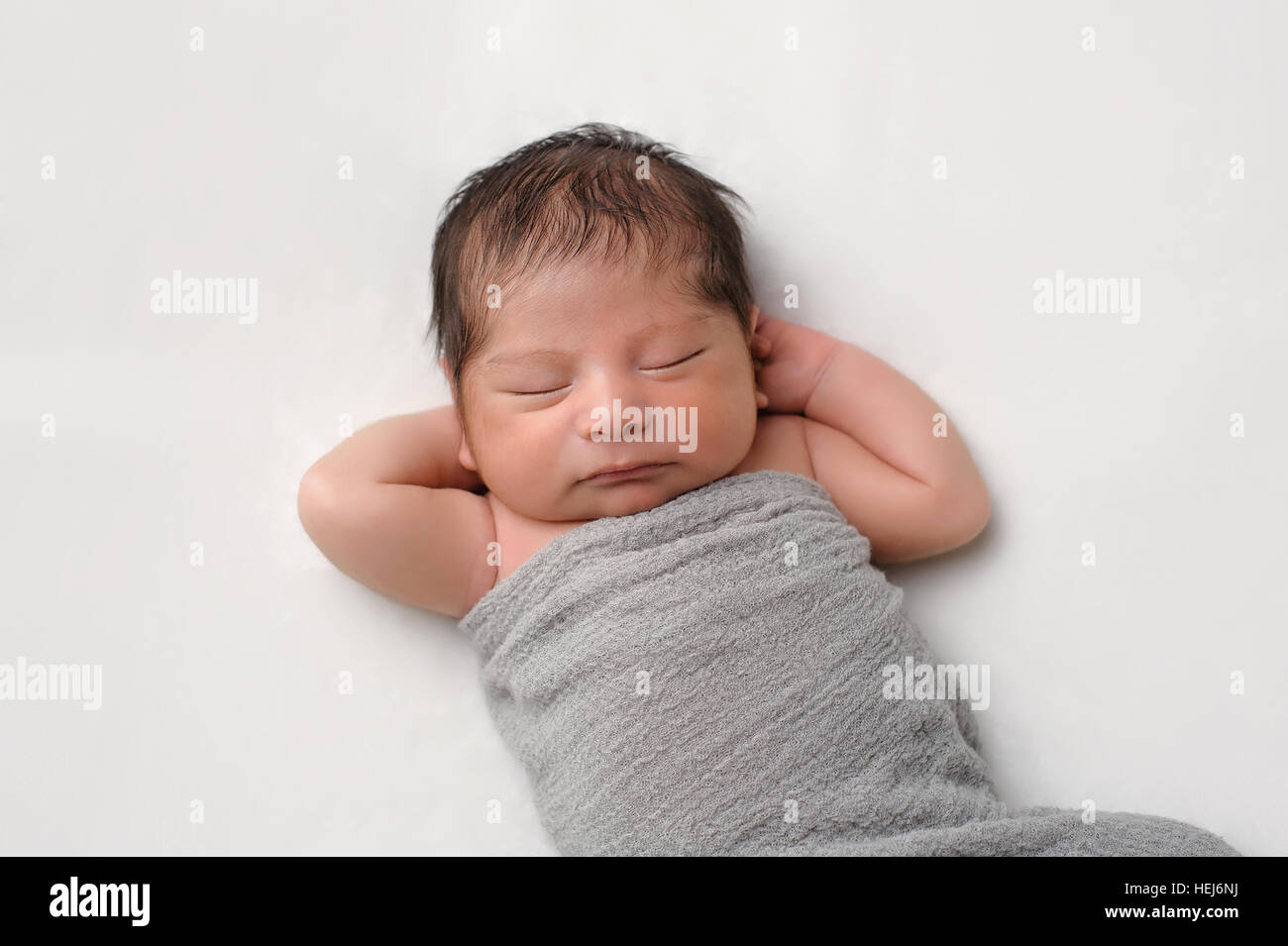Eleven day old newborn baby boy swaddled in a gray wrap. He is sleeping