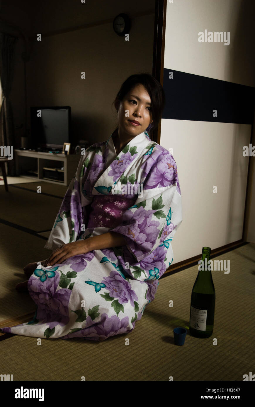 Beautiful Japanese woman in yukata (kimono)  in a traditional japanese room with a bottle of sake Stock Photo