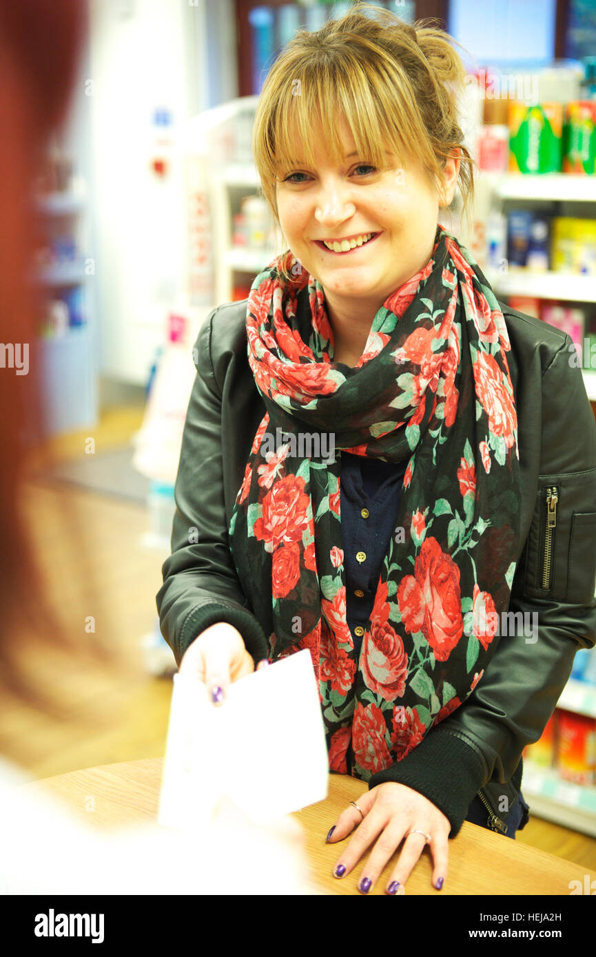 Attractive young white woman hands over NHS prescription to Pharmacy / pharmacist at the local drugs store Stock Photo