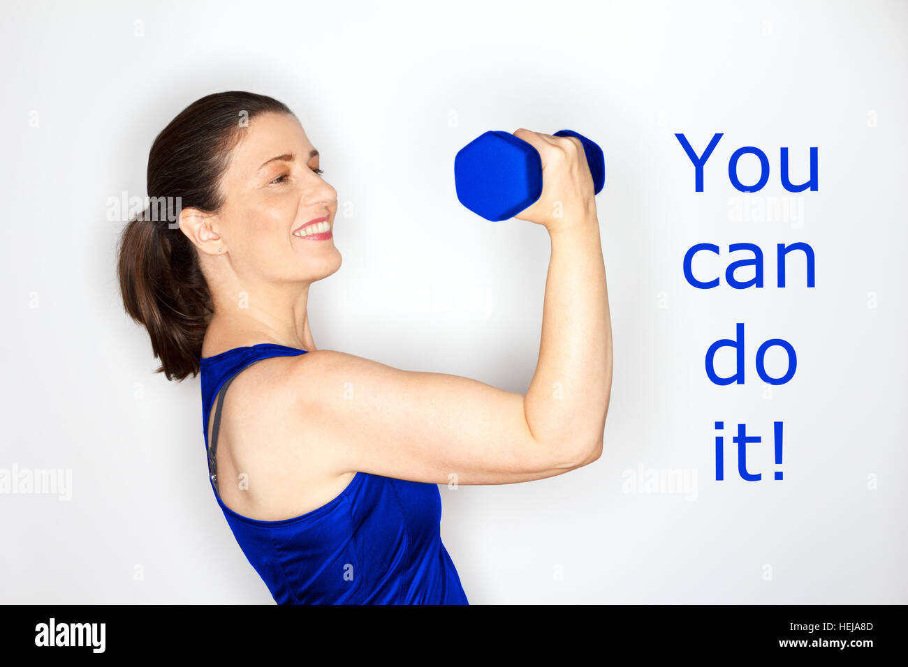 Happy and proud middle aged woman in sports outfit lifting a weight with text you can do it, blue and white, fitness, strength Stock Photo