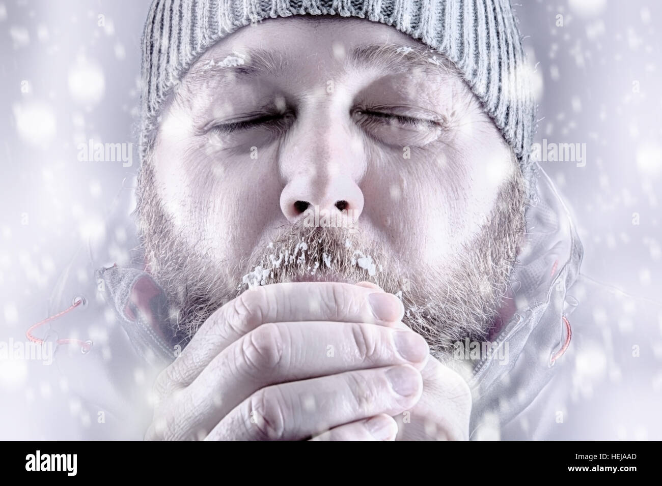 Freezing cold man in snow storm white out trying to keep warm by blowing into his hands. Stock Photo