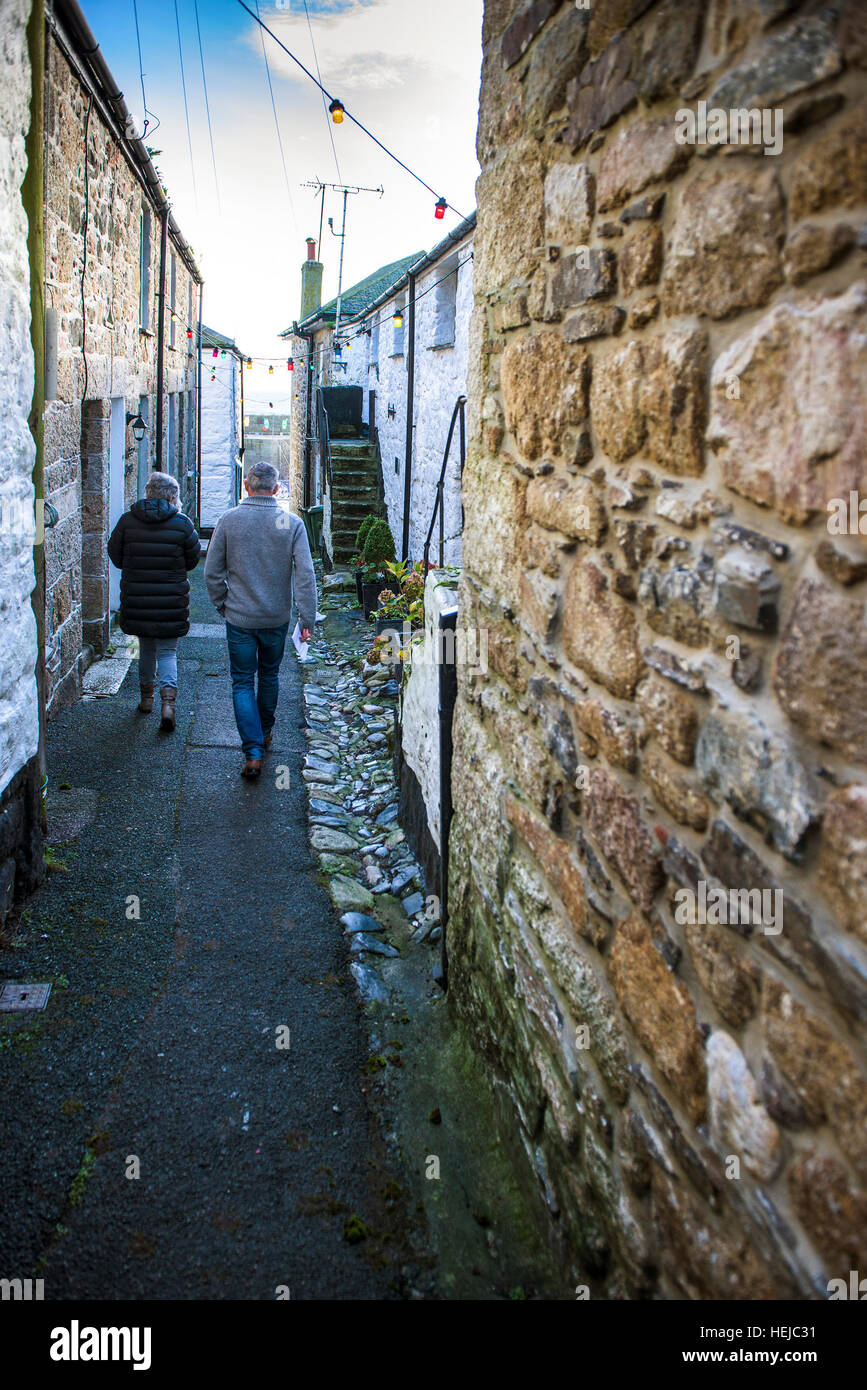 A couple walking down the quaint picturesque Duck Street in the historic village of Mousehole, Cornwall. Stock Photo