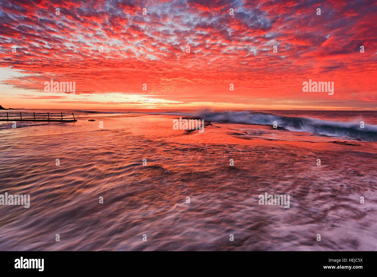 Red colourful sunrise over sea horizon at Mona Vale beach of Sydney northern beaches around rock pool. Stock Photo