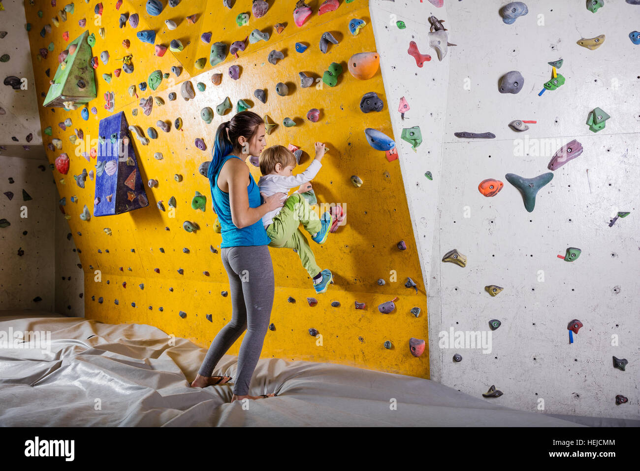 Young female bouldering instructor helping boy climb artificial wall