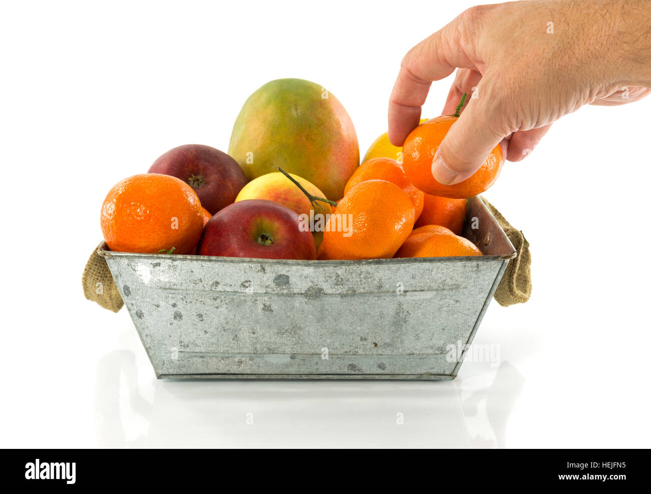 male hand taking tangerine fruit from fruit bowl with mango lemon and