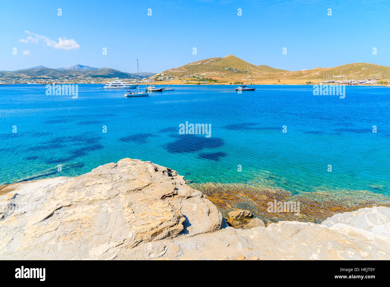 Rocks on coast of Paros island and sailing boats on azure sea water, Greece Stock Photo