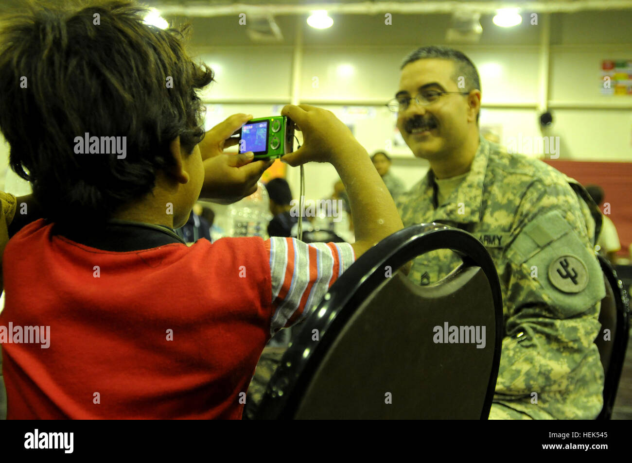 Master Sgt. Kevin Zavala, a chaplins assitant for the 103rd Sustainment Command (Expeditionary), and a Necedah, Wis., native, poses for a phots as an Iraqi boy takes a photo of him druing Iraqi Kids Day, July 31, at Joint Base Balad, Iraq. Zavala has seven children of his own and wanted to use his expereince with children to help out in this event. JBB service members host Iraqi Kids Day 307276 Stock Photo