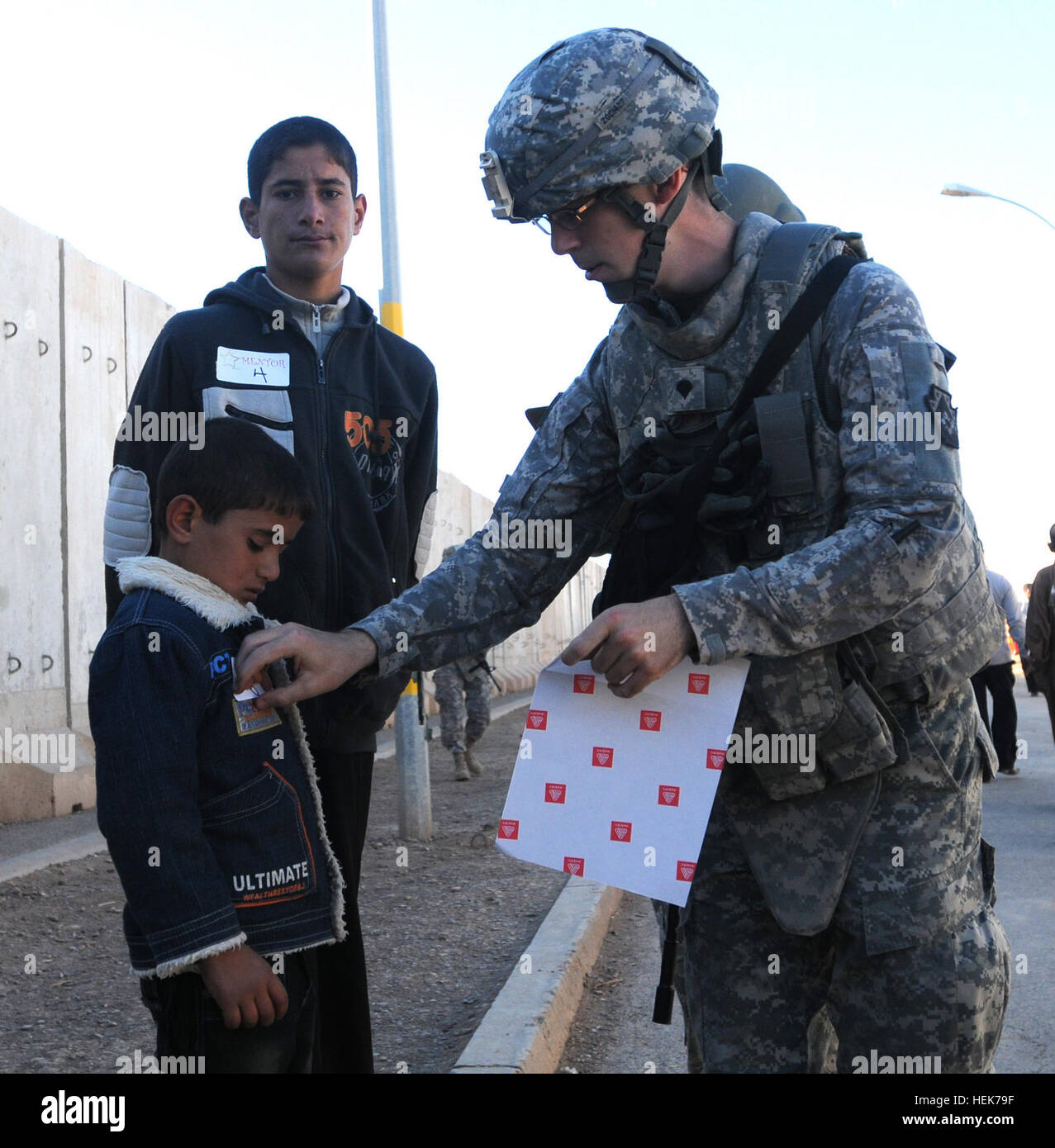 Spc. Zane Craig, public affairs specialist with the 109th Mobile Public Affairs Detachment, 103rd Sustainment Command (Expeditionary), and a Gettysburg, Pa., native, places a sticker onto a little boy's jacket allowing him access to Joint Base Balad, Iraq, during Iraqi Kids day on Nov. 5. More than 130 kids were given the opportunity to dance, play soccer, beanbag toss, and even ping-pong. Iraqi Kids Day 338190 Stock Photo