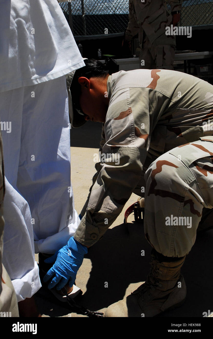 A Detention Operations Center escort assigned to the Navy Expeditionary Guard Battalion adjusts a detainee's restraints at Camp Delta. The NEGB provides a portion of the guard force at Joint Task Force Guantanamo's detention facilities. Escorting a detainee 237296 Stock Photo