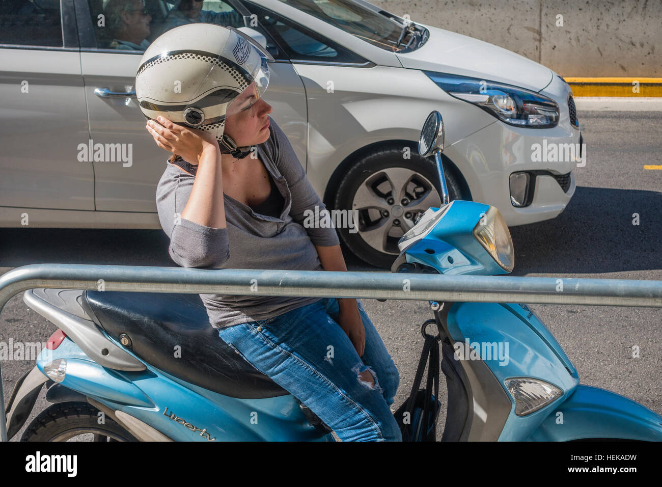 A female motor scooter driver stuck in traffic leans against a railing