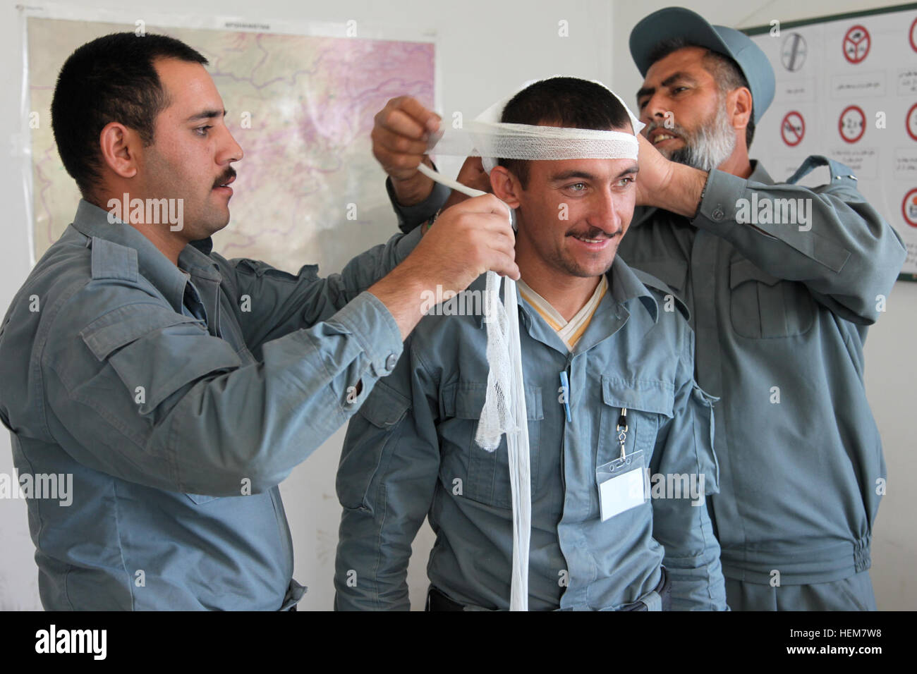 An Afghan Uniform Police instructor, right, and one of his recruits, left, demonstrates the proper way to apply a head bandage onto another recruit, center, during first aid training at Forward Operating Base Shank, Logar province, Afghanistan, July 7, 2012. (U.S. Army photo by Sgt. Austin Berner) AUP first aid training 120707-A-BZ540-021 Stock Photo