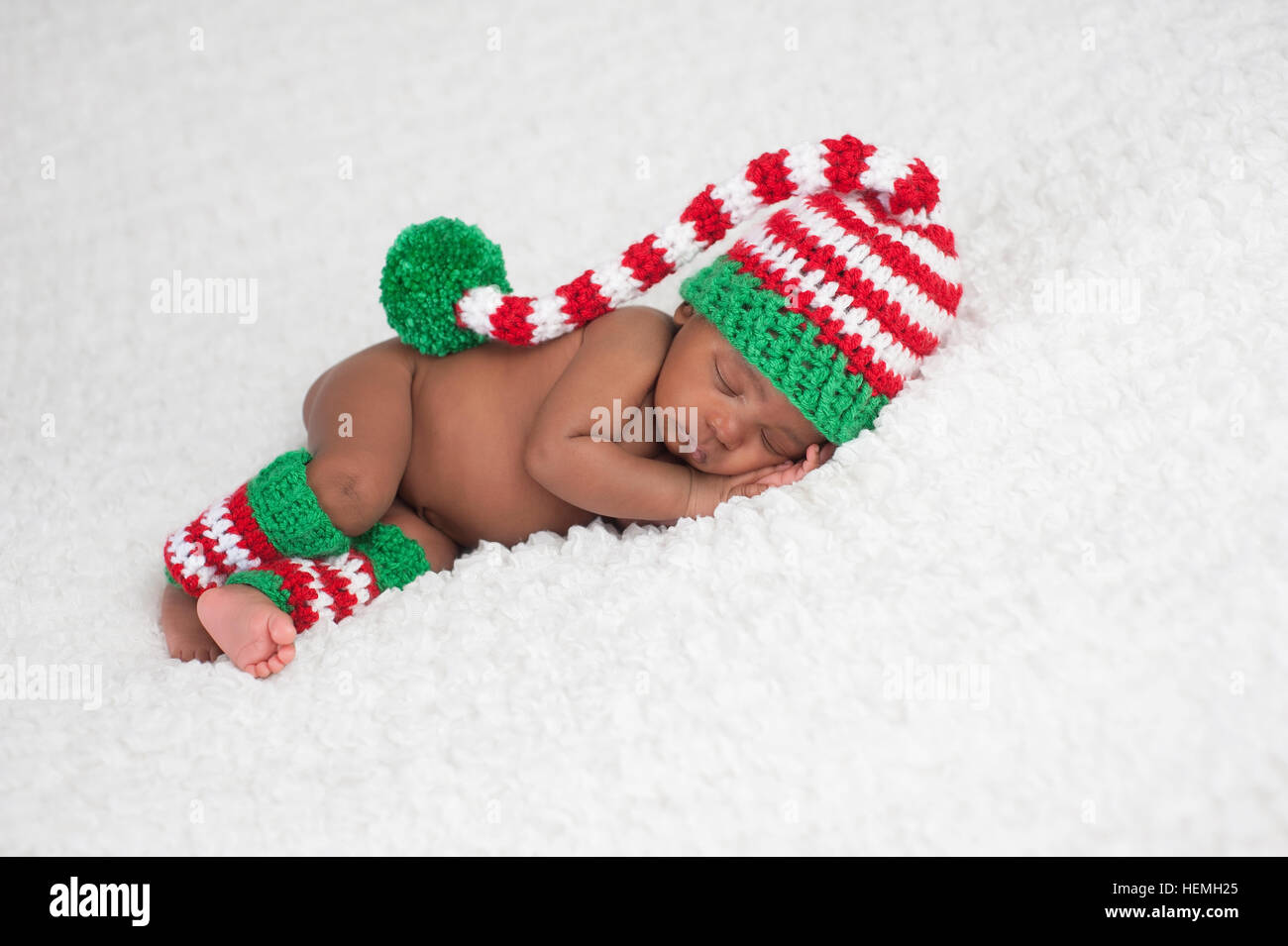 A one month old baby girl wearing a crocheted, red, white and green stocking cap and matching leg warmers. Photographed on a white, fluffy blanket. Stock Photo