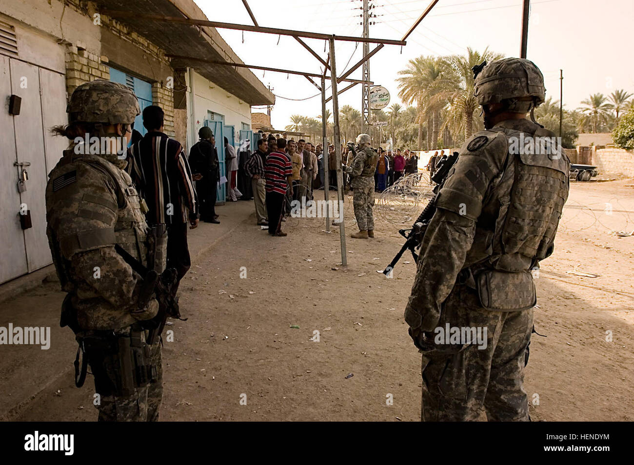 Two Soldiers from the 411th Military Police Company, 716th MP Battalion, 18th MP Brigade, Multi-National Division – Baghdad observe as Sons of Iraq (Abna al Iraq) line up outside a shop in Abayachi March 2. Soldiers from the 411th MP Co. pull security to support the mission of Company B, 1st Battalion, 14th Infantry Regiment, 2nd Stryker Brigade Combat Team, “Warrior,” 25th Infantry Division, MND-B to pay SOI volunteers from the Abayachi area, north of Baghdad. Soldiers support payday activities 79509 Stock Photo