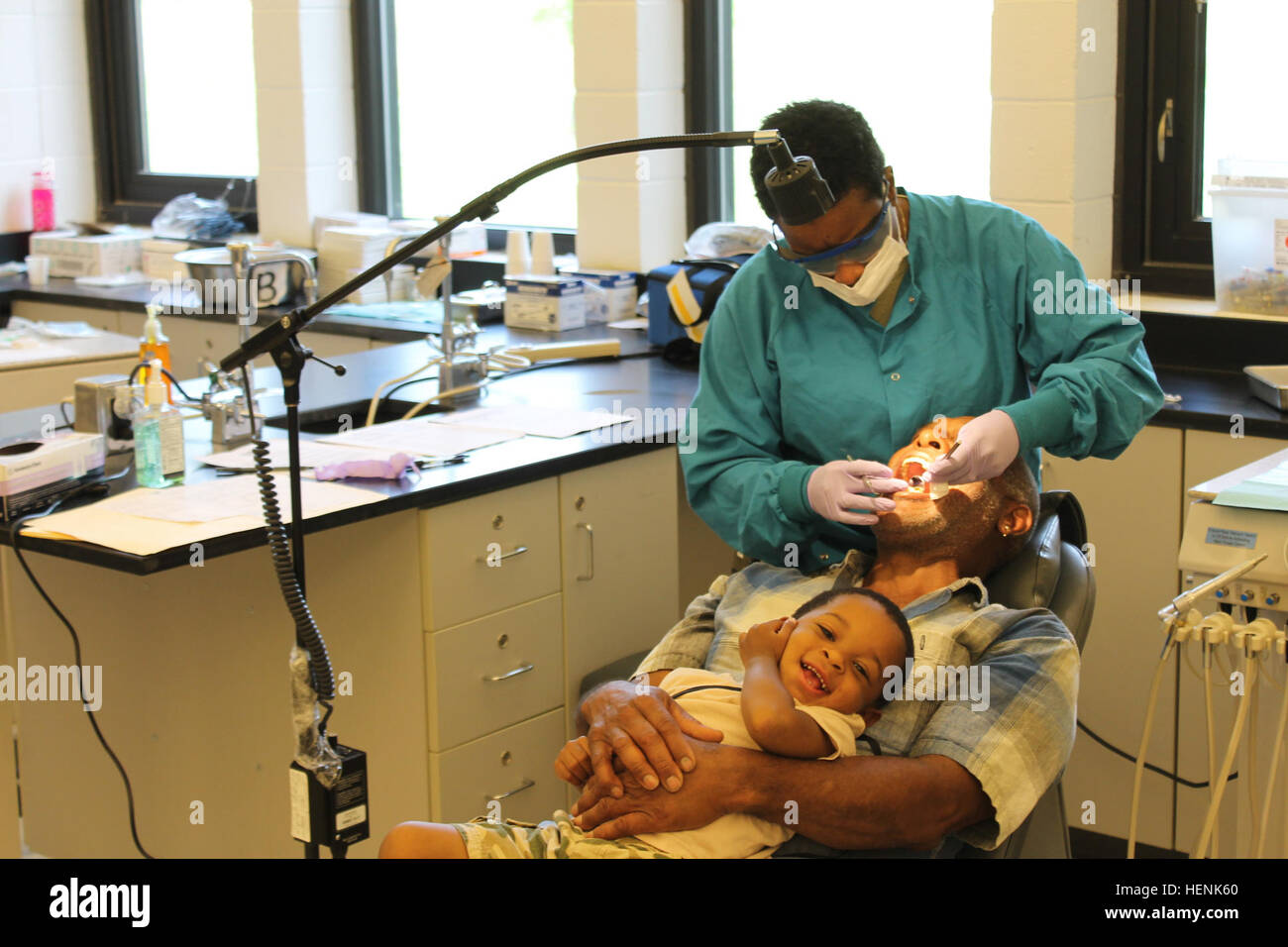 Sgt. 1st Class Nicole Lawrence, a dental hygienist with the 810th Medical Company (Detachment), 49th Multifunctional Medical Battalion out of Charleston, S.C., and the NCOIC of the Harrisburg dental clinic for Innovative Readiness Training exercise Southern Care 2014, examines the teeth of Don Wilkins of Harrisburg, while his son De'Mere, 2, laughs on his lap. The purpose of the civil-military program IRT SC14 is to improve military readiness while providing quality medical services at no cost to residents of Southern Illinois. Southern Care 2014 140620-A-VL725-004 Stock Photo